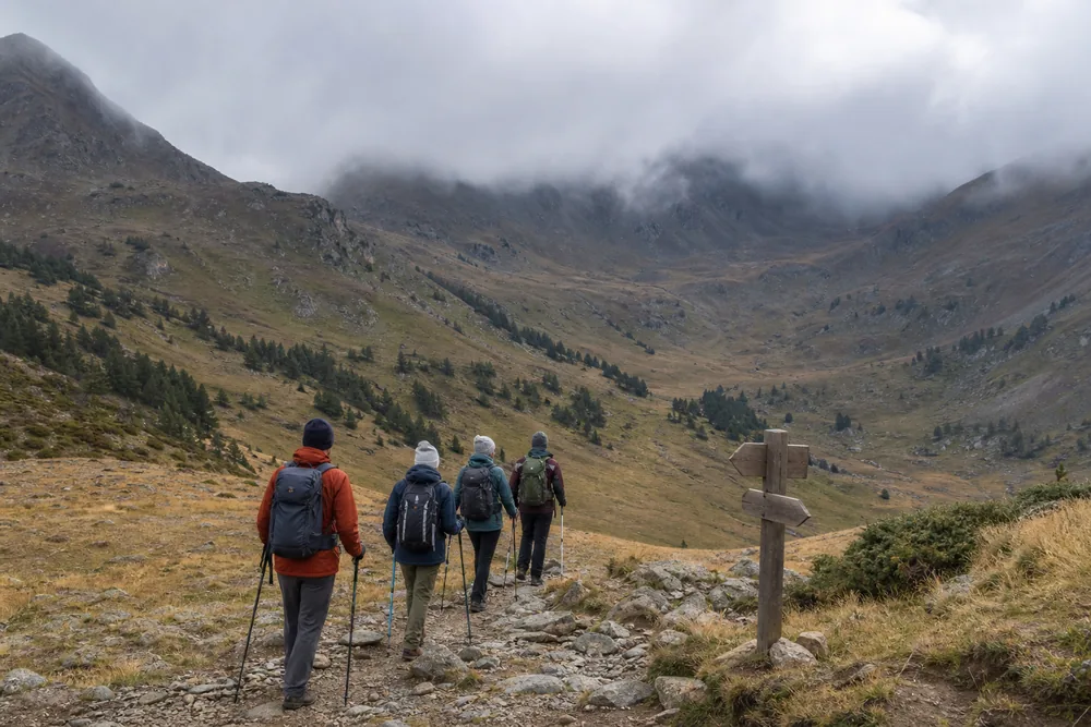 Trekking group turns downhill from a marked decision point as cloud covers a generic mountain pass - Mountain pass turnaround | KnowOutdoor