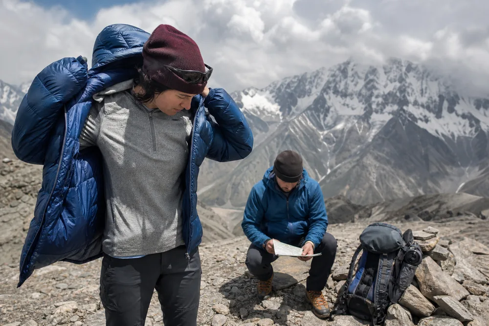Trekker pulls a warm insulated jacket over dry active layers immediately after reaching a windy pass - Stop layer transition | KnowOutdoor