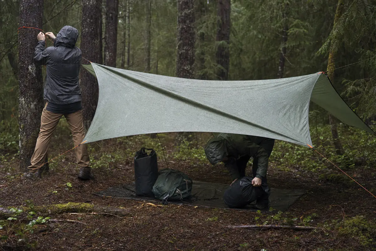 Trekkers building tarp cover before opening dry clothing and sleeping gear - wet camp setup | KnowOutdoor